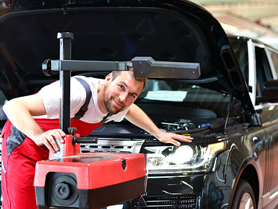 Ein Mechaniker steht vor einem geöffneten Motorhaube eines Autos und lächelt.