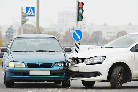Zwei kollidierte Autos an einer Kreuzung, das blaue Auto vorne links und das weiße Auto rechts.